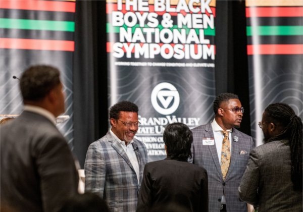People stand talking in front of vertical banner, The Black Boys and Men National Symposium