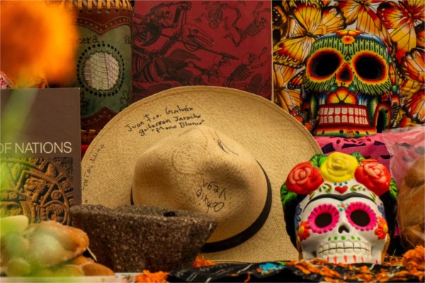 Offerings and decorations on GVSU's ofrenda, including a hat with a message on it and decorated skulls.
