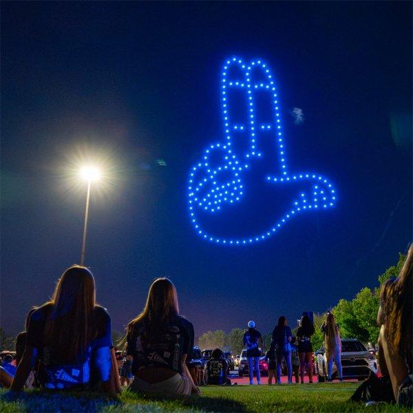 The GVSU "Anchor Up" symbol is part of a drone show. People are sitting and standing while watching the drone show.