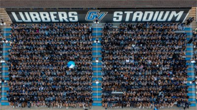 GVSU students are seen from above sitting in Lubbers Stadium. The words Lubbers Stadium are on the back wall. Cheerleaders line the stairs. A blue and aqua beachball is over one part of the crowd.