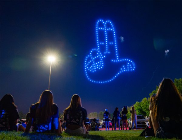 A drone dhows the GVSU "Anchor Up" symbol. People are sitting and standing to watch the drone show.