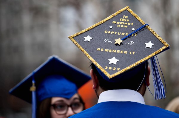 A student wearing a graduation cap that reads "In this moment now, capture it, remember it". 