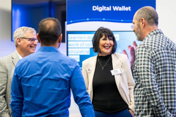 A person smiles while talking with three other people. The words "Digital Wallet" in the background.