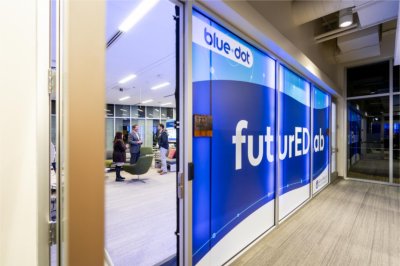 A sign with different shades of blue is seen in windows to a glassed-in office area. The signs contain the words "blue dot" and "futureEDlab."