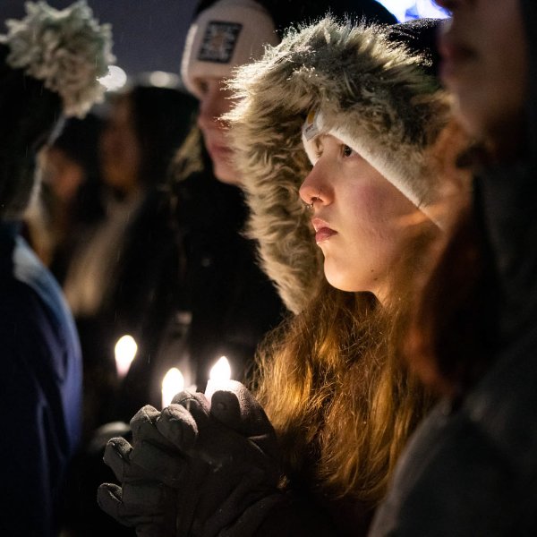 A college student wearing a warm coat is illuminated by candlelight during a vigil.