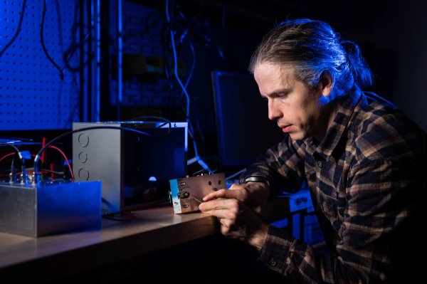 A person works on a small metal box in a university lab setting.