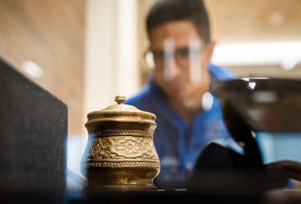 A student is seen looking through glass covering an antique metal object.  