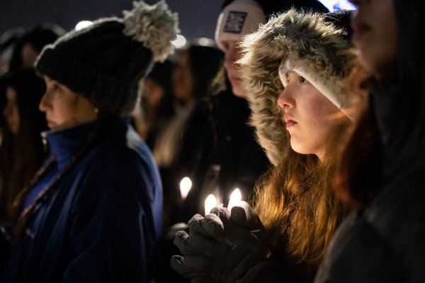  A college student wearing a warm winter coat is illuminated by candlelight during a vigil. 