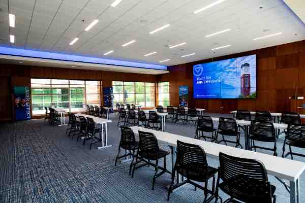 The Laker Experience suite with three rows of tables and chairs is pictured; in front is screen with carillon tower and words: Ready for Whatever is Next