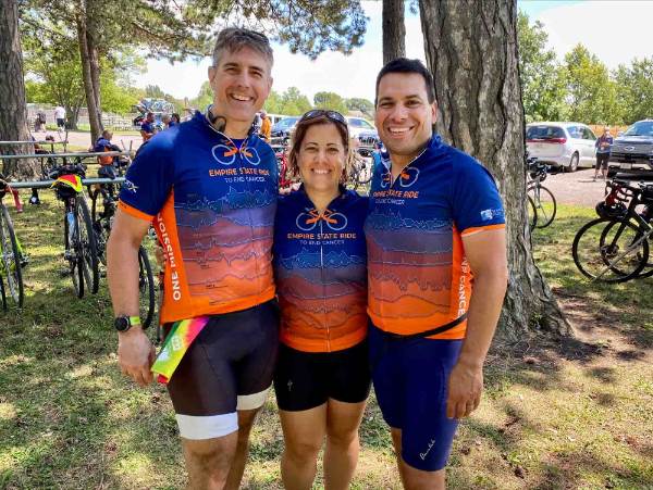 three friends stand in front of tree in bicycle shorts and shirt that designate them as Empire State Ride participants