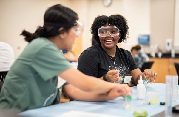 Two students laugh together while wearing safety googles. 