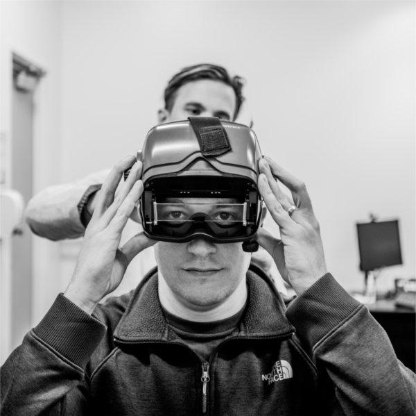 Justen Knape, a graduate student, dons immersive headset in the community hearing clinic with the help of Colton Clayton standing behind him