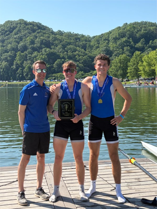 Kyle Barnhart, left, stands on a dock next to two GVSU rowers, one holding a plaque