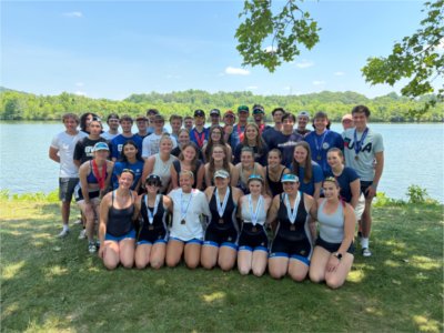 GVSU rowing team standing in front of river, some with medals around their necks