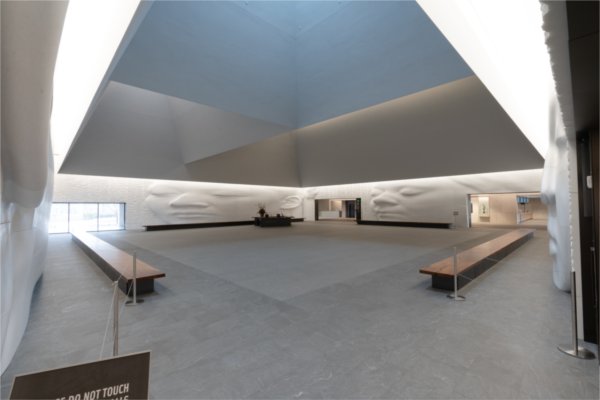 A space with benches and a sculpture on faces on the wall.