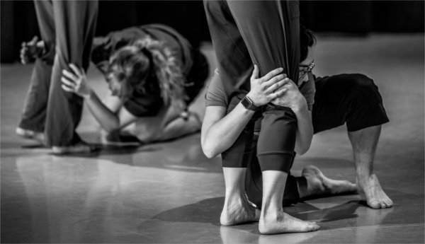 Dancers kneeling on the floor embrace the lower legs of other dancers.