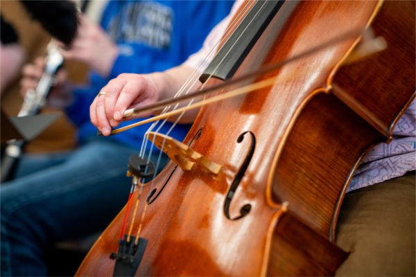 A closeup of a person playing a cello. The person's hand is seen drawing a bow across the strings.