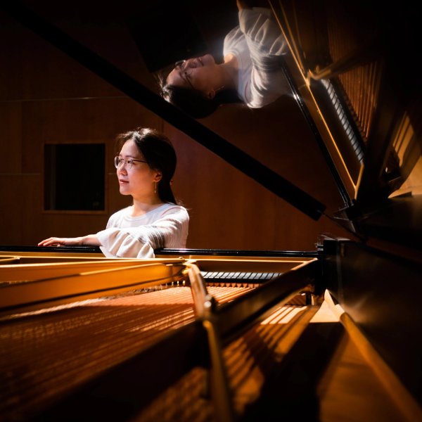 Sookkyung Cho stands near a piano, which also reflects her image.