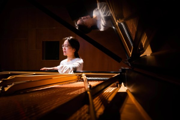 Sookkyung Cho stands next to a piano, which also reflects her image.