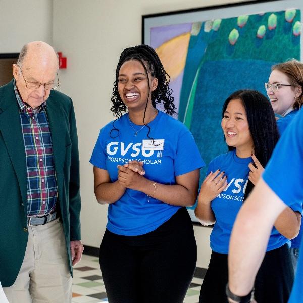 Bob Thompson looks down as three Thompson Scholar students applaud.