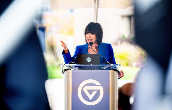 GVSU President Philomena V. Mantella stands behind a podium with a GVSU logo while speaking during an event.