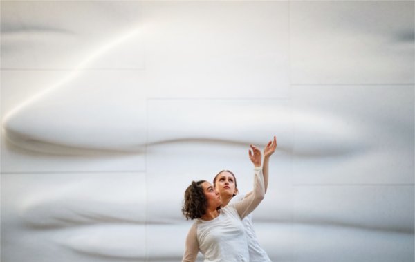 Two dancers wearing while perform in front of a white face sculpture. 