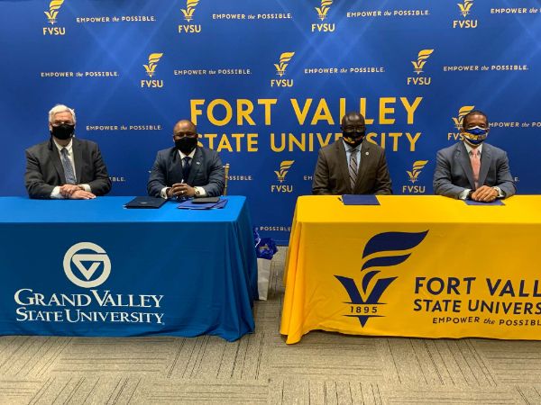 four people in masks seated at tables in front of sign at Fort Valley State University.