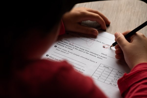 A child, photographed from the back, writes on a piece of paper.