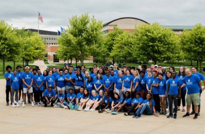 large group of students, faculty and staff all wearing blue GVSU Oliver Wilson Scholar t-shirts; pictured with Student Services Building behind them