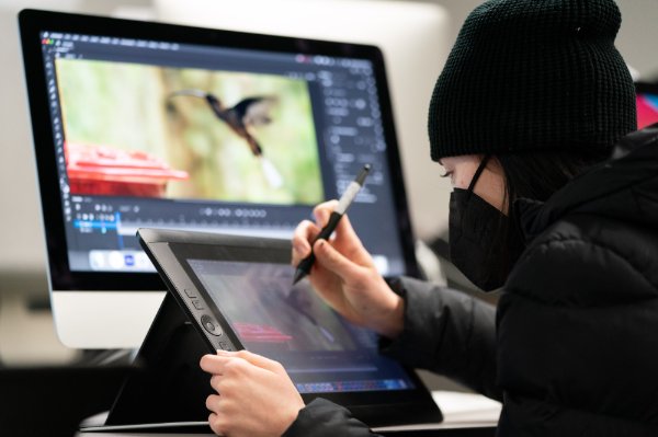 A student, wearing a mask, draws a bird on the computer screen.
