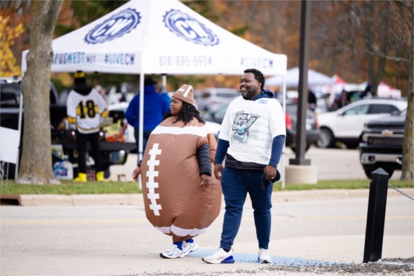 A man and a woman, who is wearing an inflatable football costume, walk around the Homecoming tailgate.