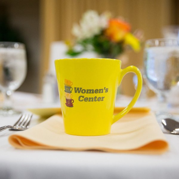 A yellow mug on a table setting that reads "Women's Center"