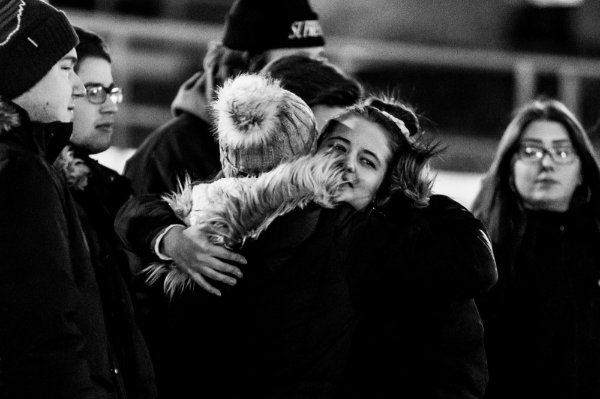 Black and white image of two people in coats and hats embracing.