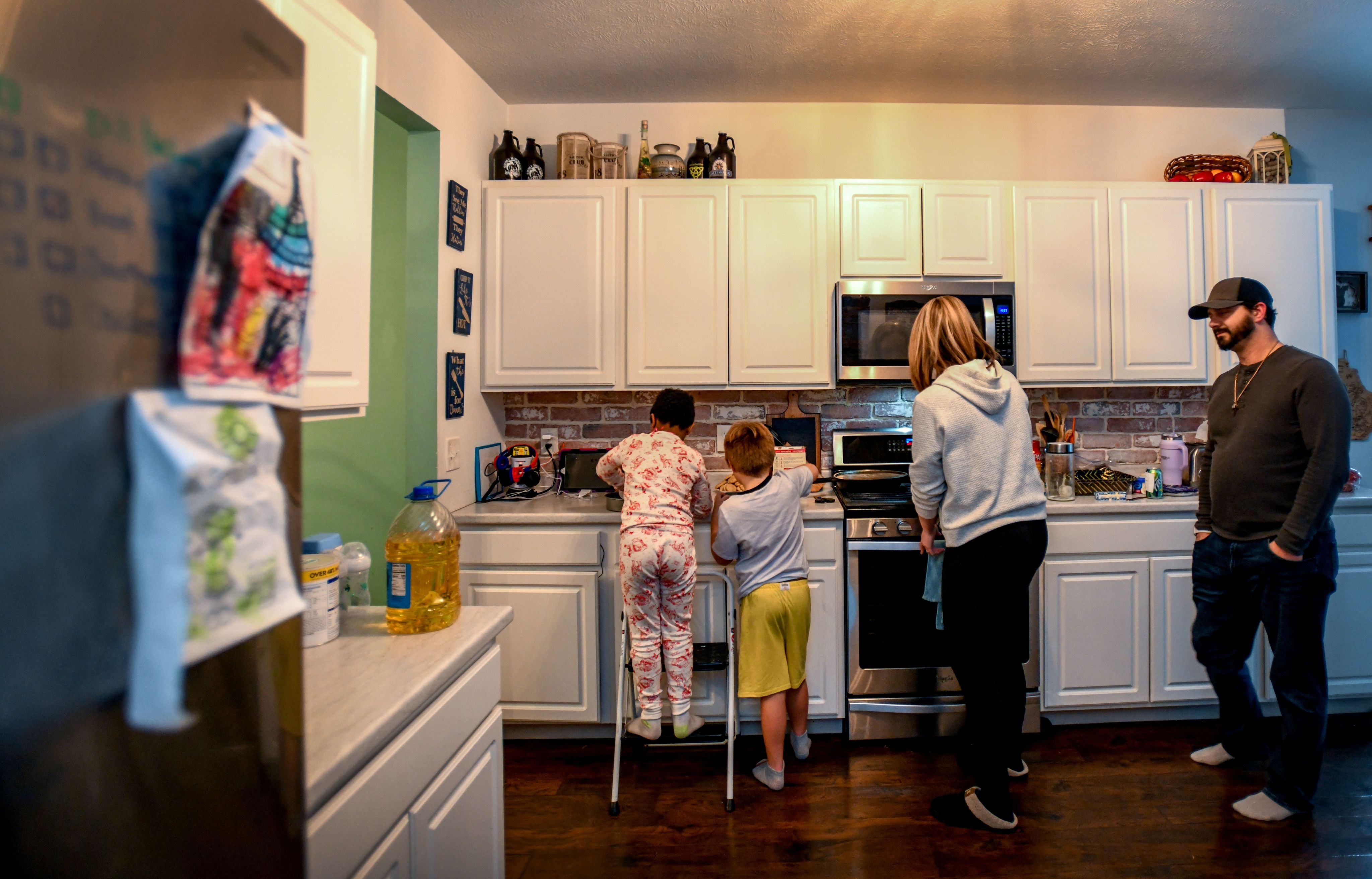 Four individuals stand in a kitchen facing away from the camera.