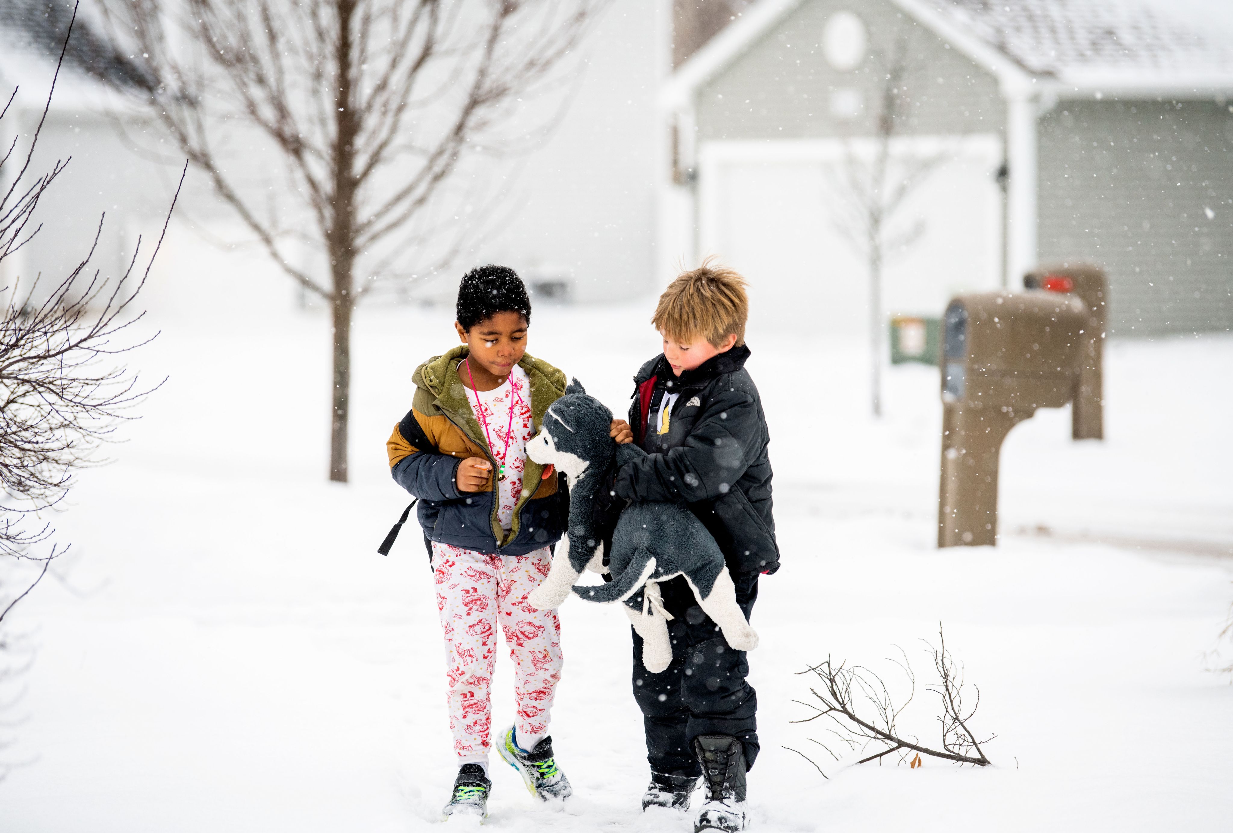 Two children hold a stuffed animal while walking outside in the snow.