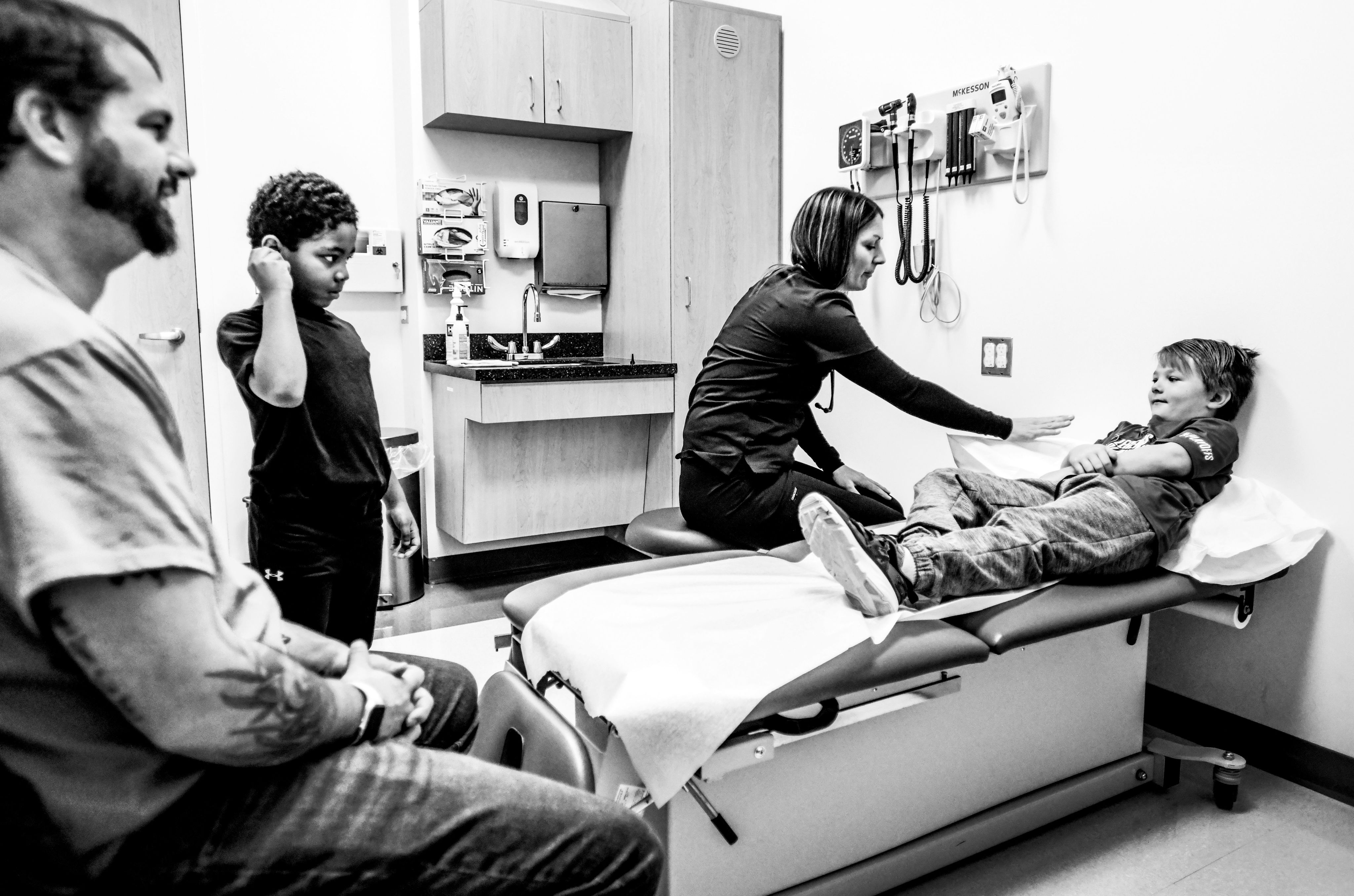 A black and white image of a child laying on an examination table while others watch on.