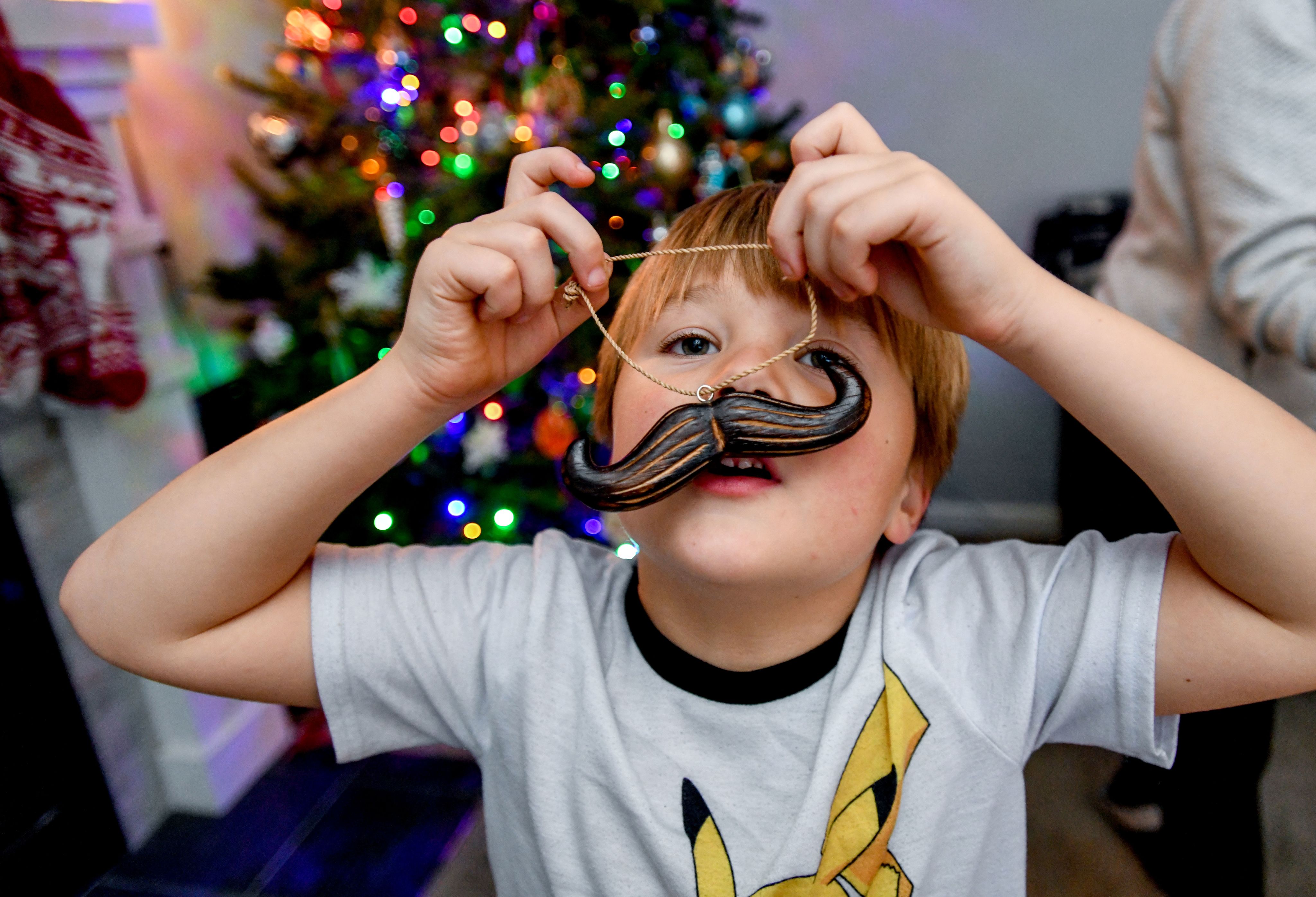A child holds a mustache ornament up to their face.