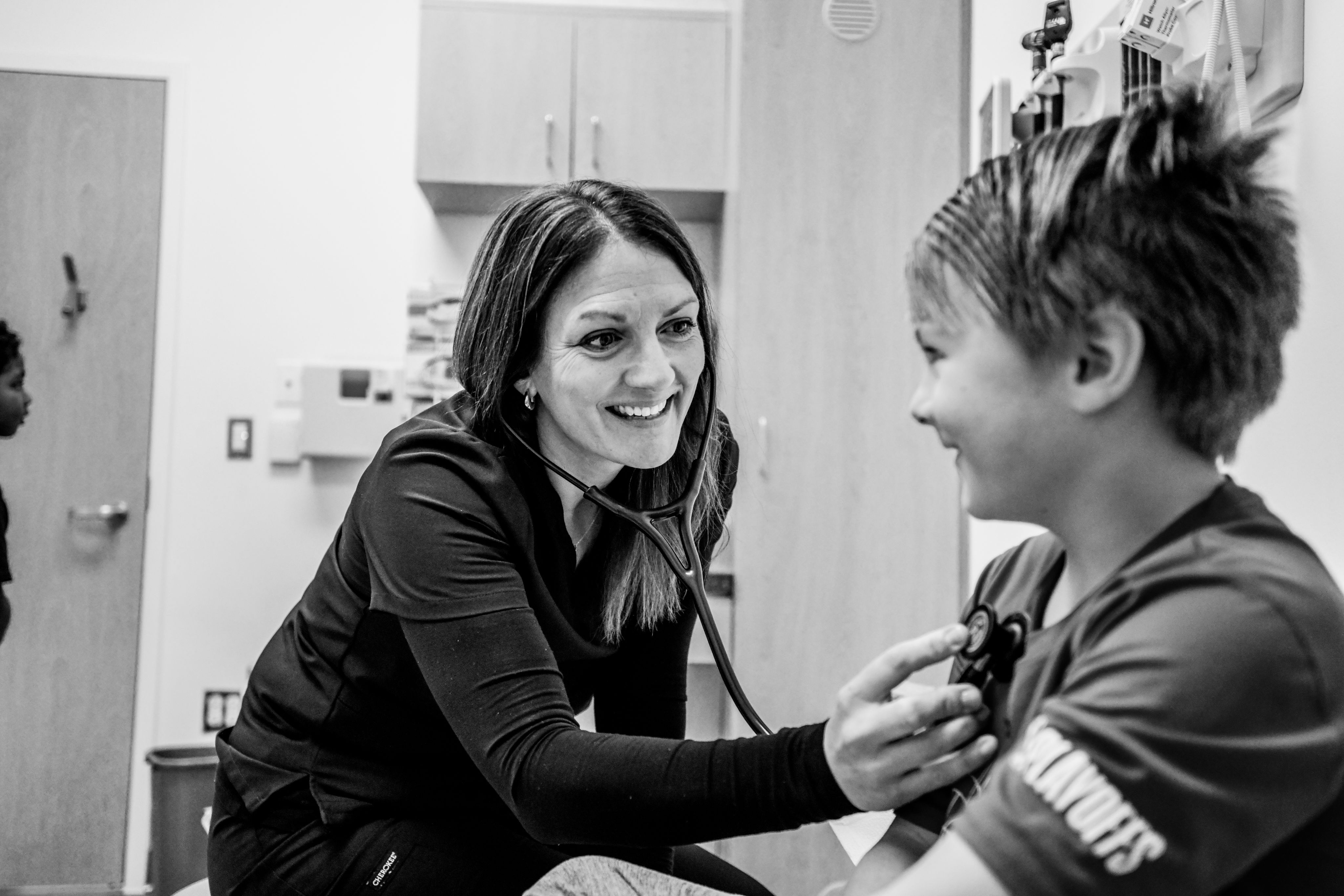 A black and white photo of a person holding a stethoscope up to a child's chest. 