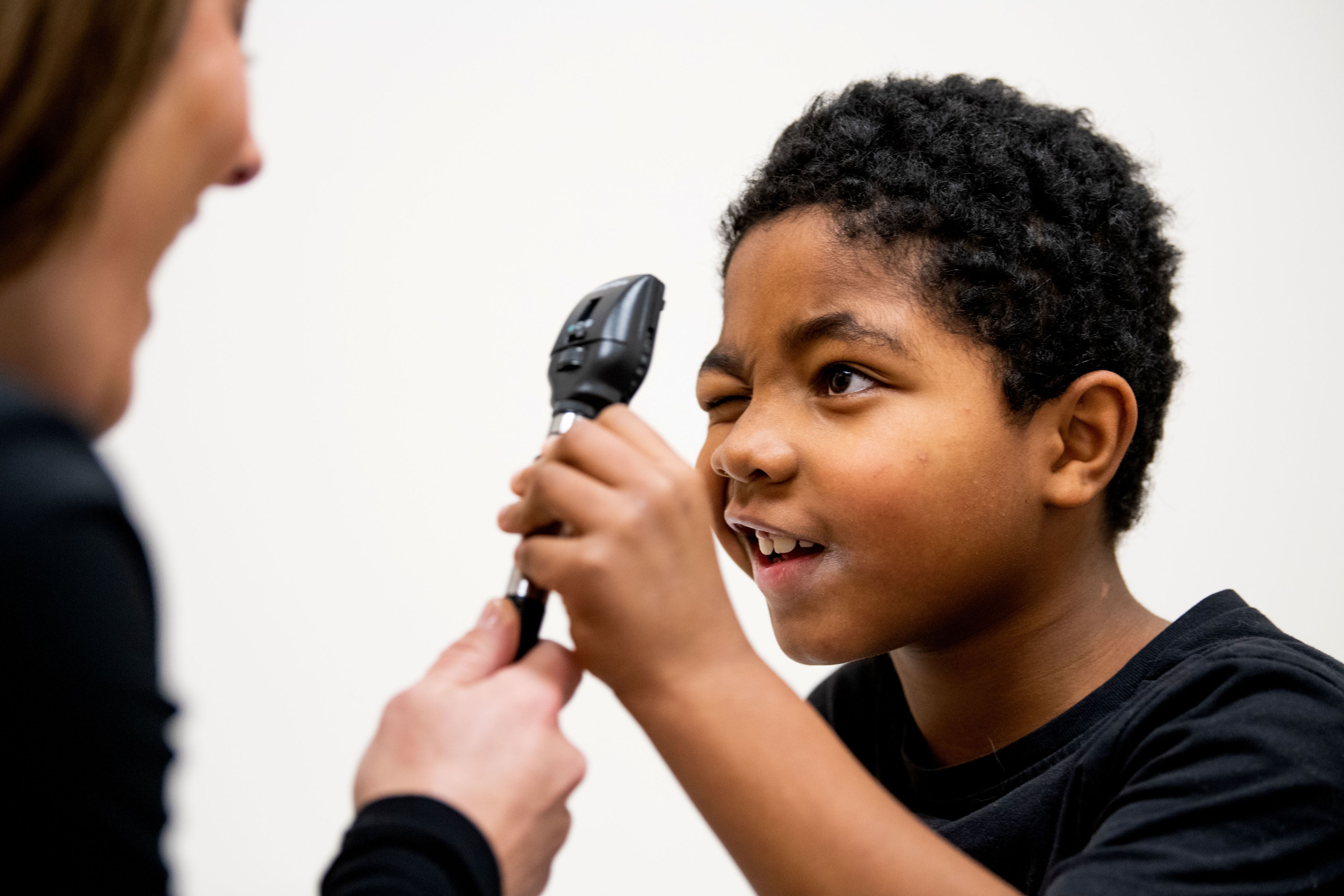 A child squints one eye closed while looking through an eye examination tool.