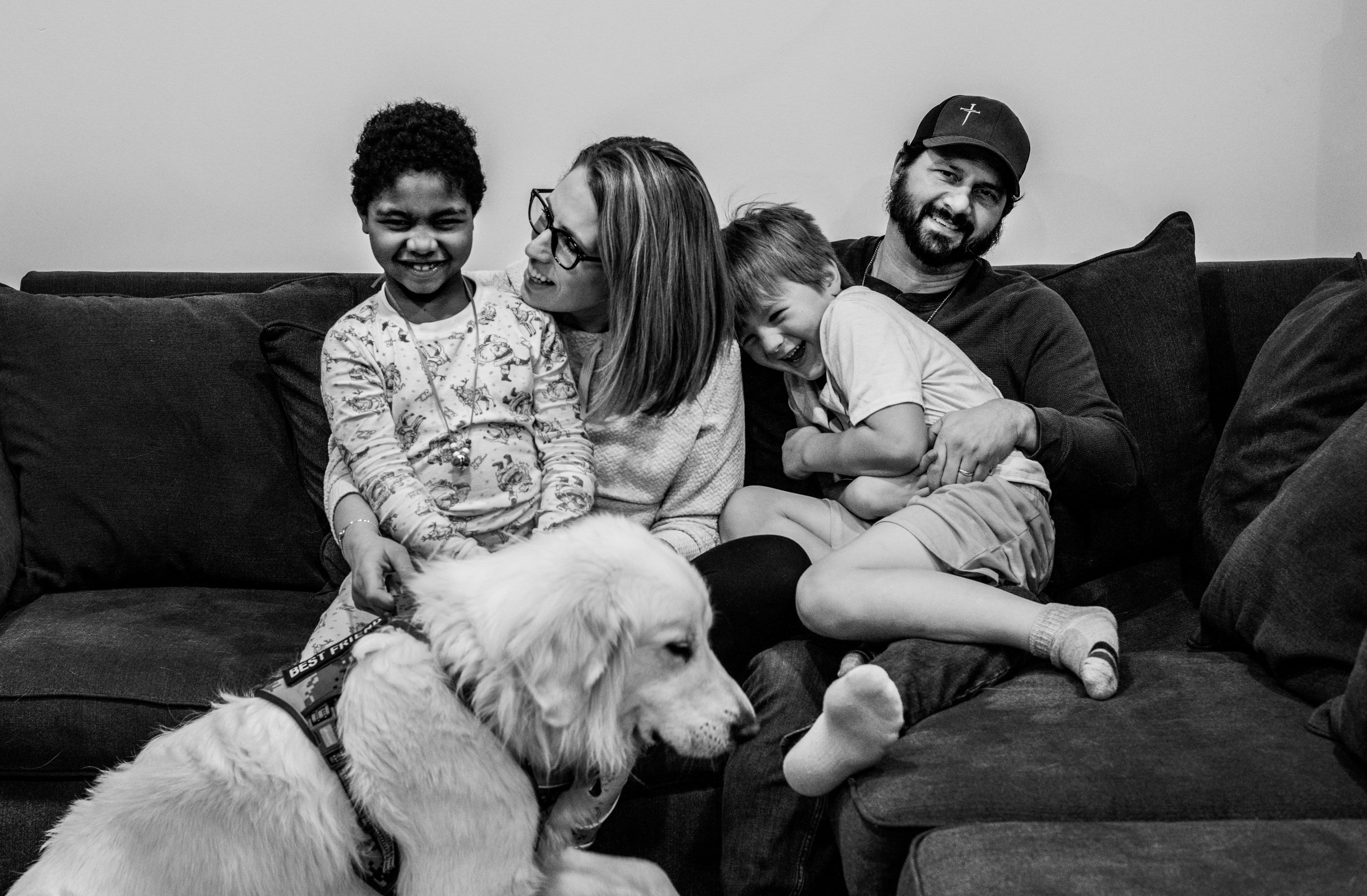 A black and white image of a family smiling together on a couch.