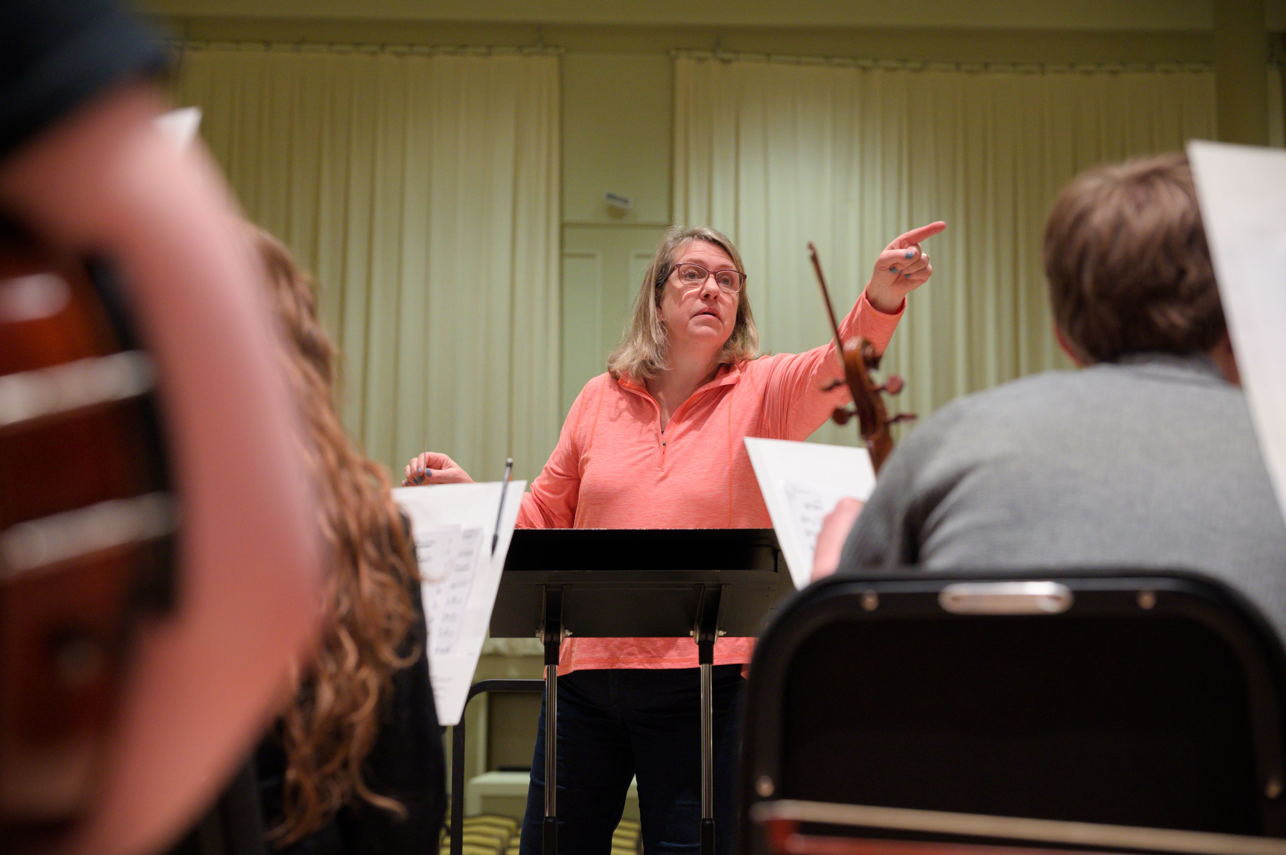 orchestra director in peach shirt giving cues on stage