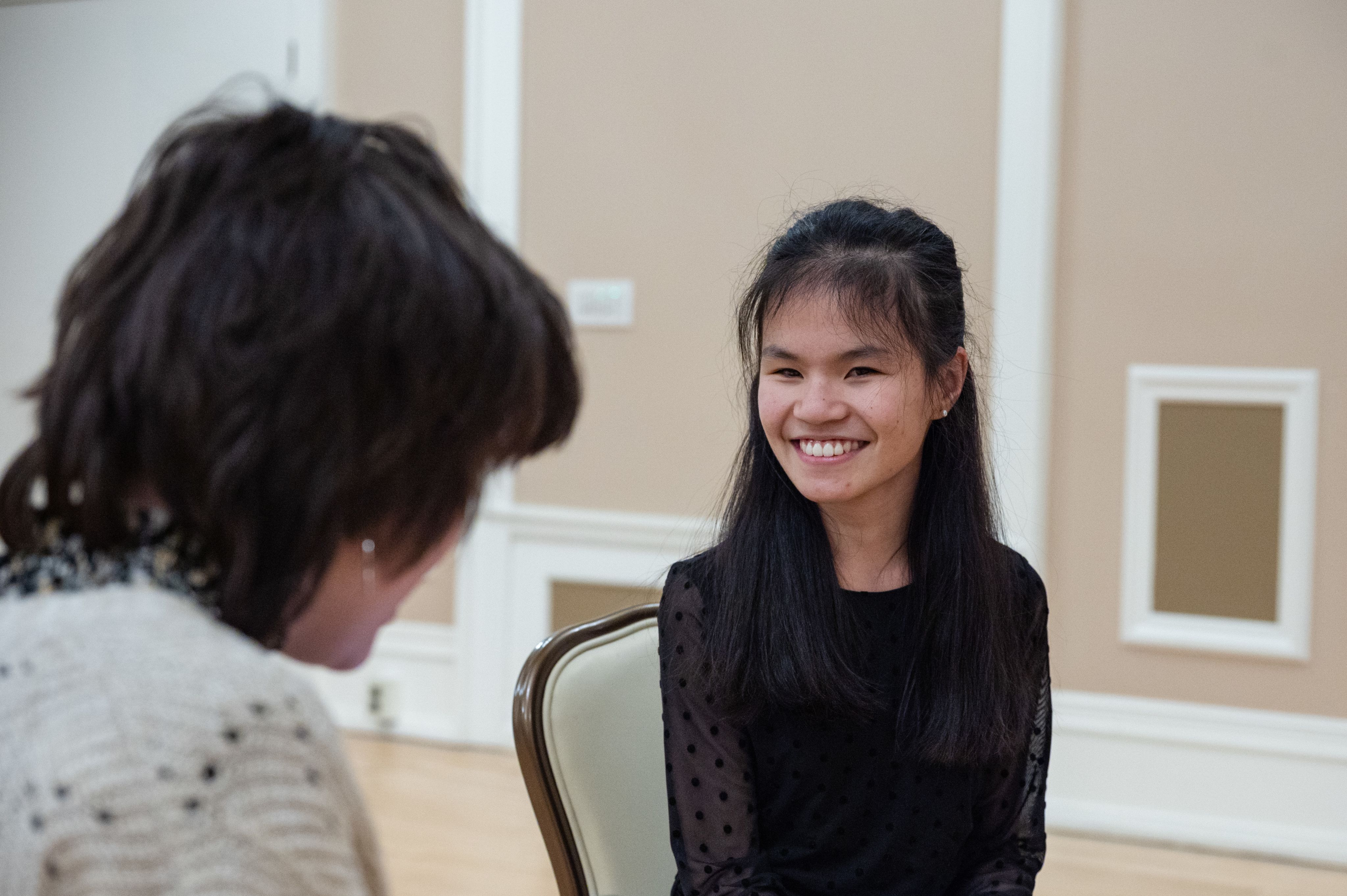 student in black smiling at another person in a white sweater, cannot see the face of the person in white