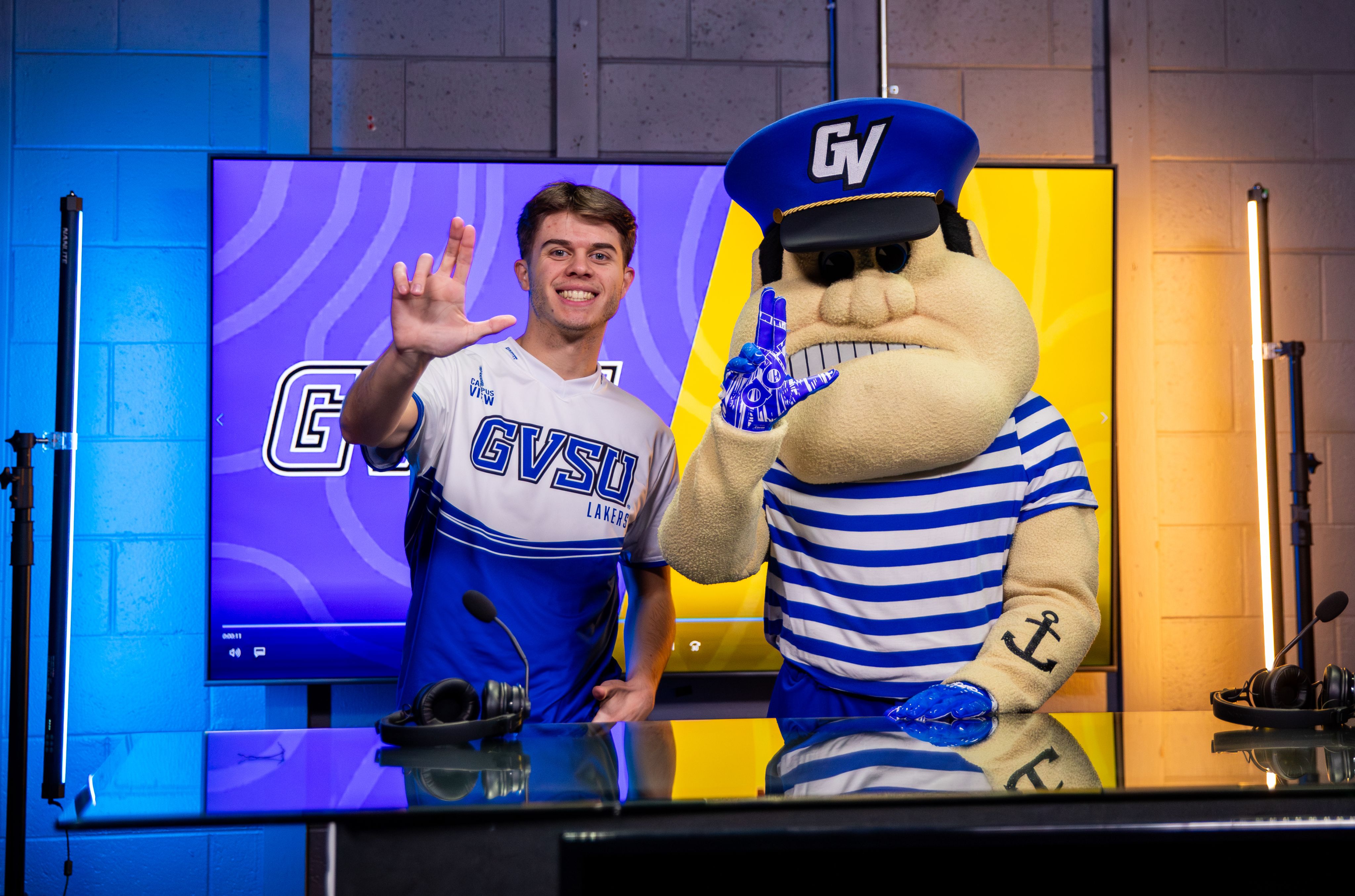 student giving anchor up sign, next to Louie the Laker