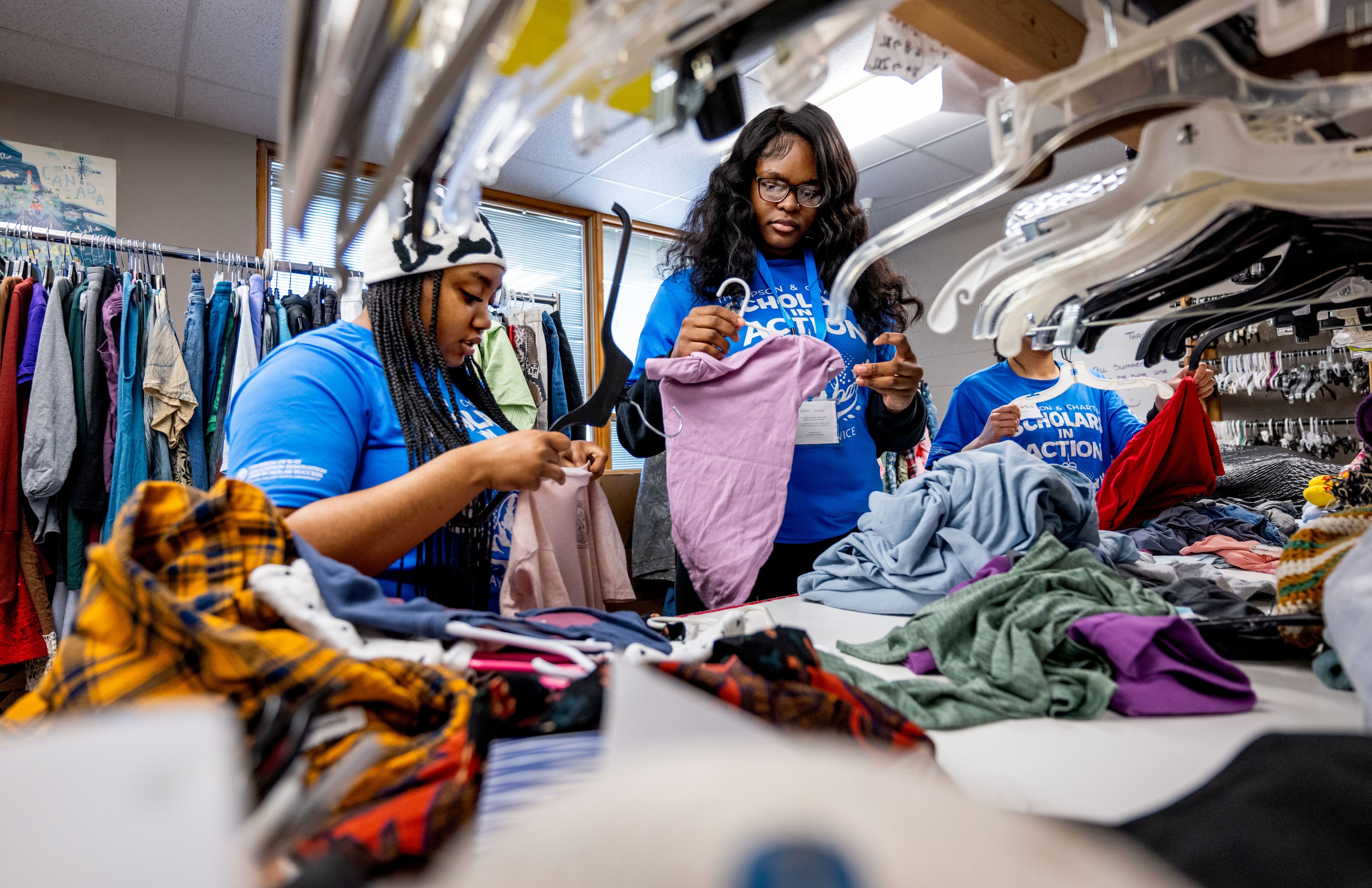 two students in blue tshirts sort clothes at a resale shop