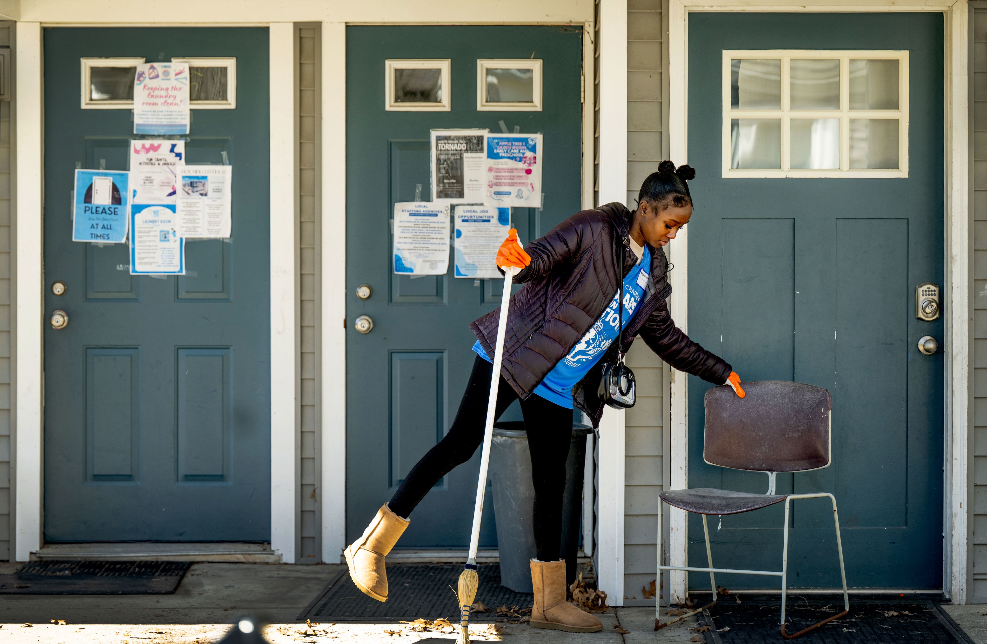 student in black winter coat with broom outside a building with three doors