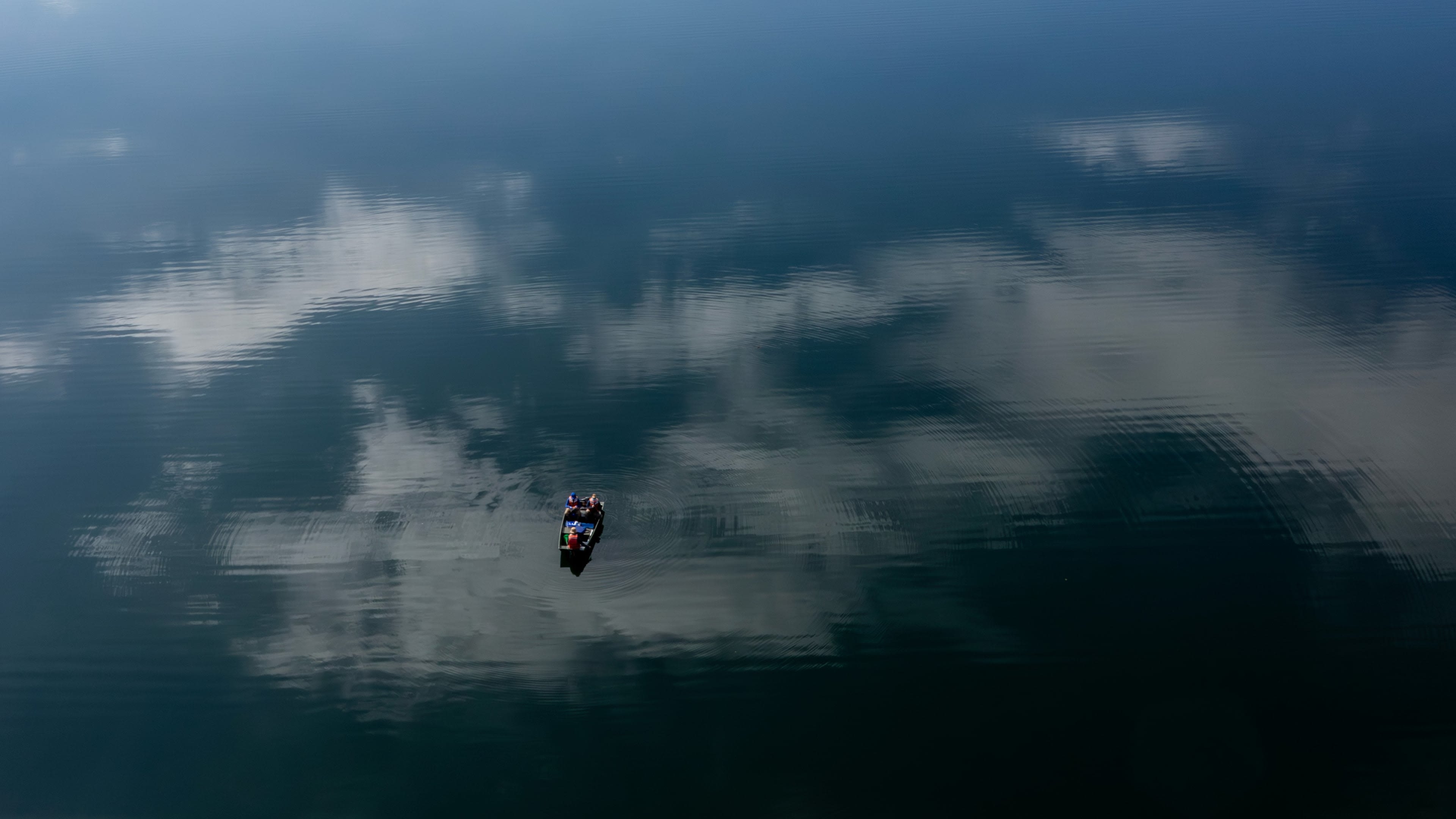 Aerial view of a group of people sitting in a boat on the lake. Clouds are reflected off the water's surface.