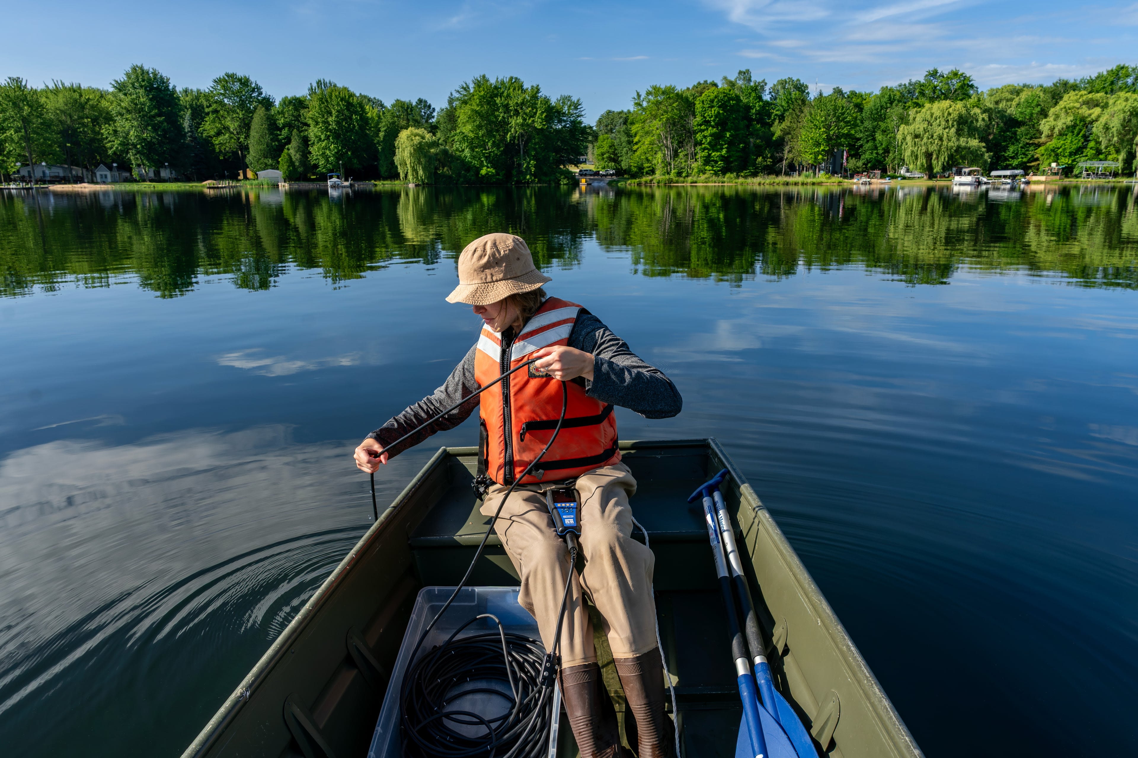 A person sitting at the end of a boat lowers a rope into the water.