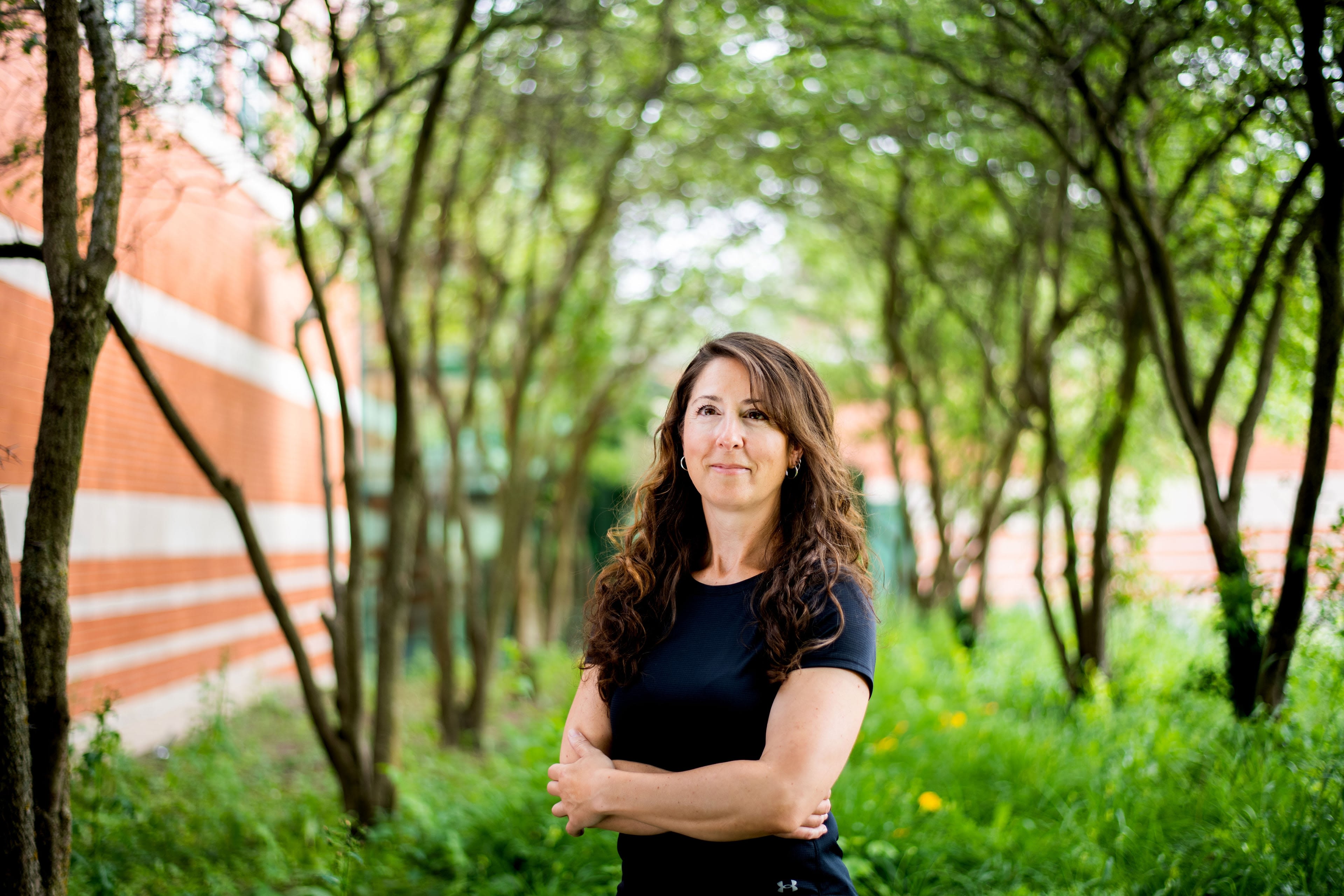 A person stands in front of buildings and trees with their arms crossed.