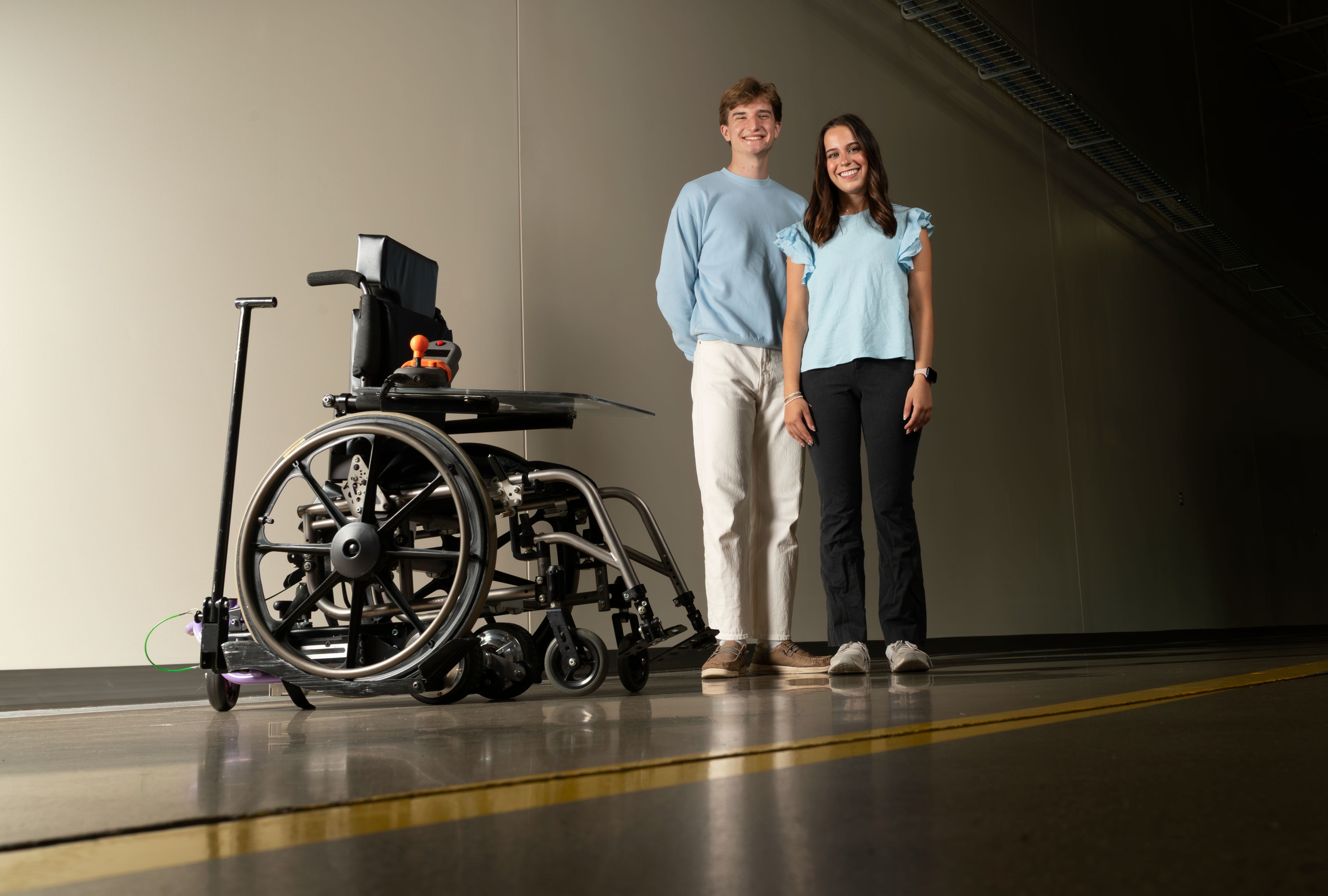Two people stand next to a modified wheelchair.