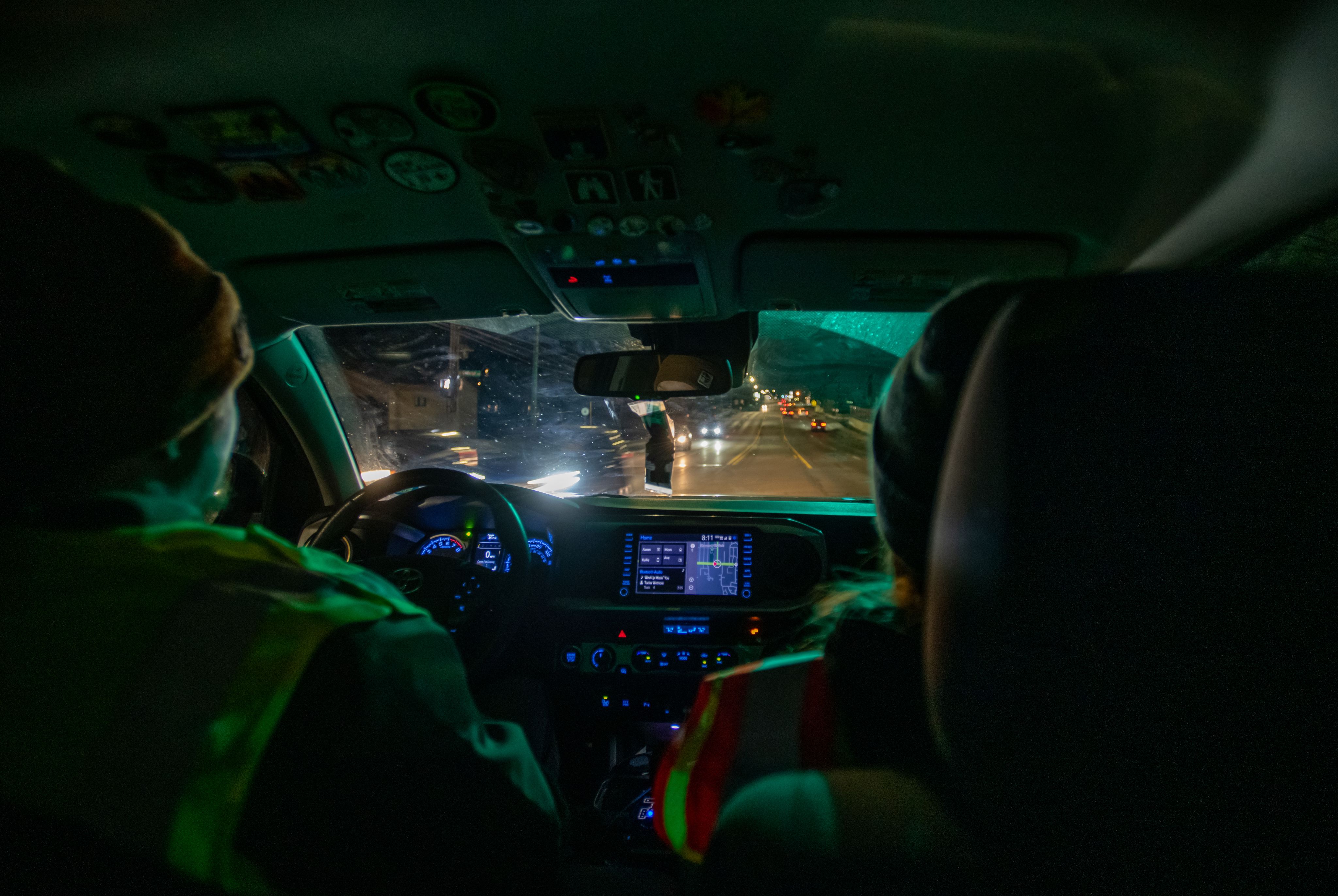 A close-up view from the inside of a car, showing two people driving at night.